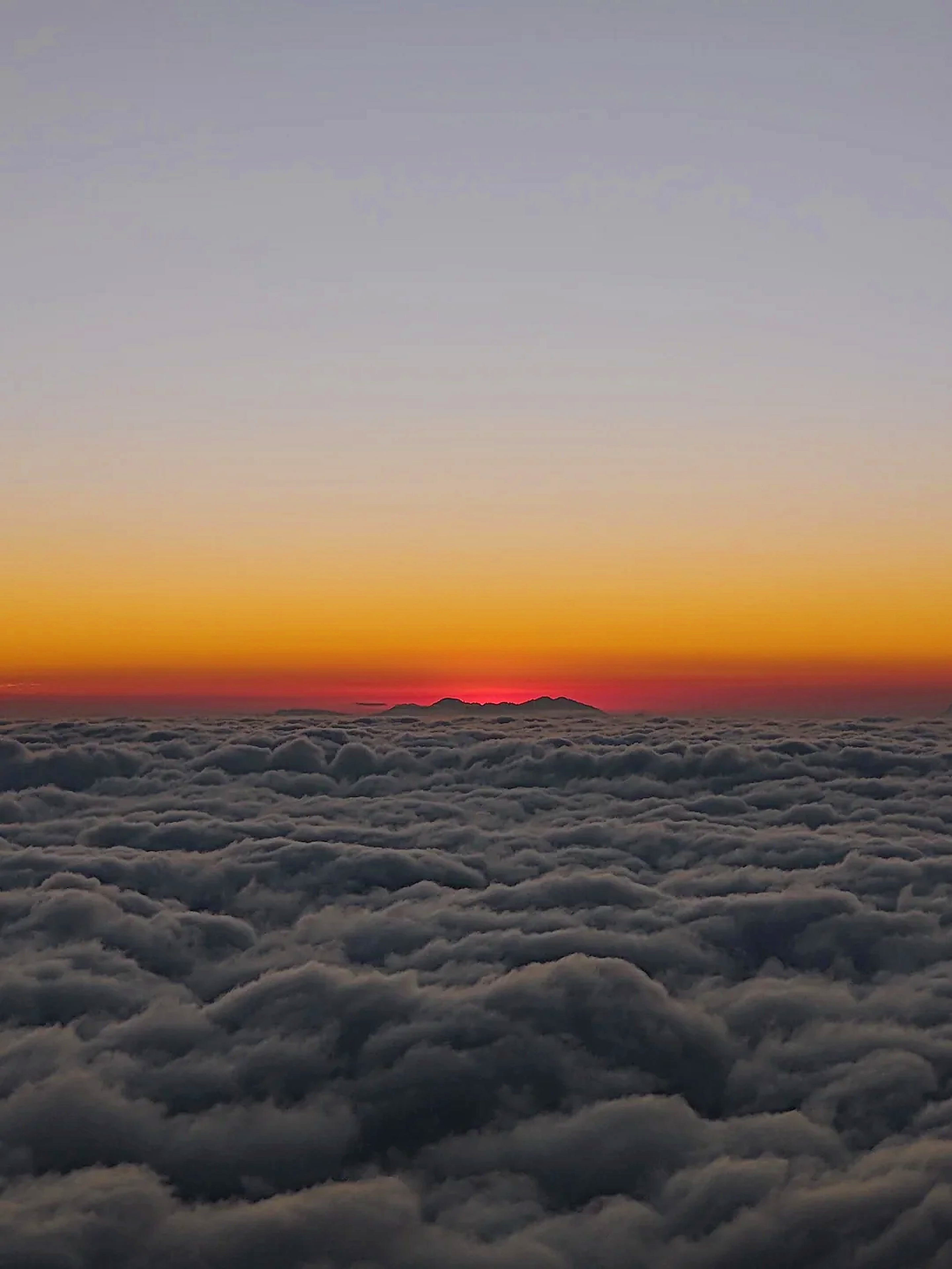 Crimson sunset over rolling sea of clouds beneath high Himalayan ridgelines